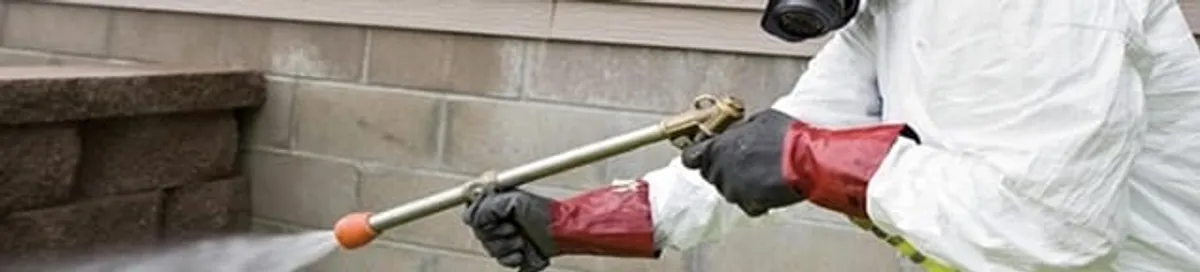 Pest control technician applying exterior insect treatment along a home foundation in Kansas City, KS
