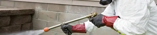 Pest control technician applying exterior insect treatment along a home foundation in Kansas City, KS