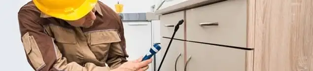 Roach exterminator applying treatment under kitchen cabinets in Kansas City, KS