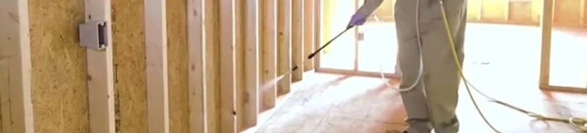 Termite treatment technician applying spray along framing and unfinished walls in Kansas City, KS