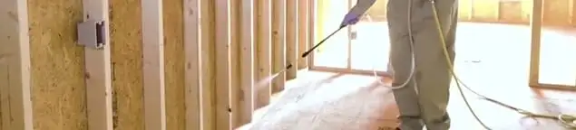 Termite treatment technician applying spray along framing and unfinished walls in Kansas City, KS