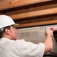 Termite inspection technician checking a basement wall and framing for termite activity in Kansas City, KS